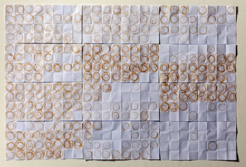 12 sheets of paper arranged to make a calendar. Each sheet has been folded into squares, with each square and used as a coaster for a single day. Ring-shaped coffee stains visualise daily coffee consumption over the year, which is greatest in May and least in December.